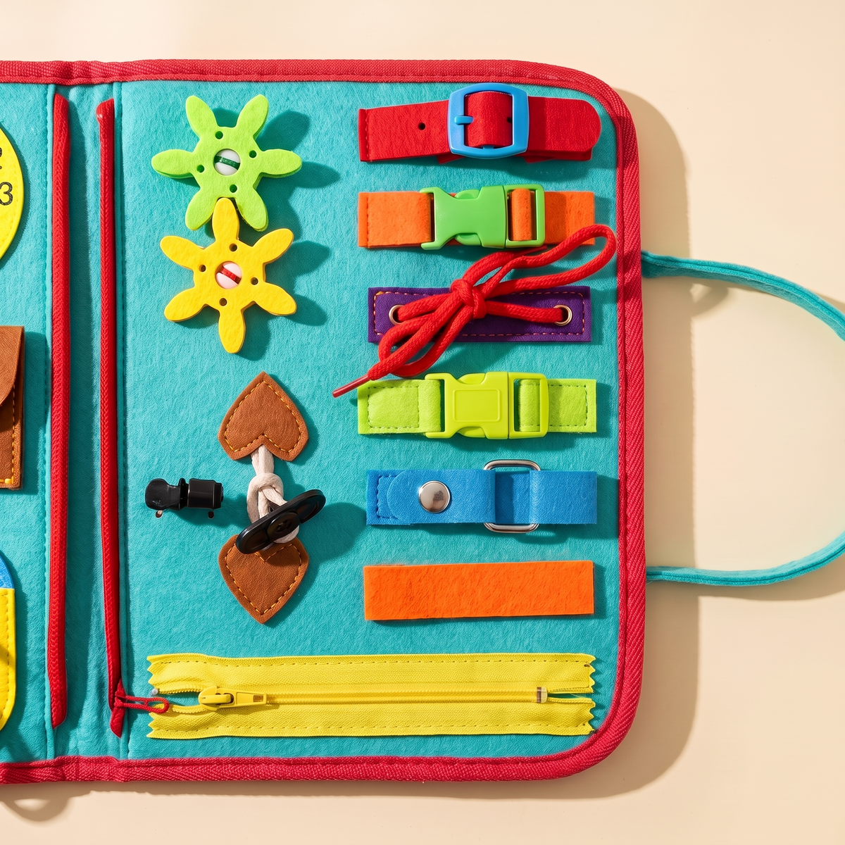 Close-up of the busy book's right-hand page: yellow zip, coloured buckles and straps, a red lace and toggle fastenings